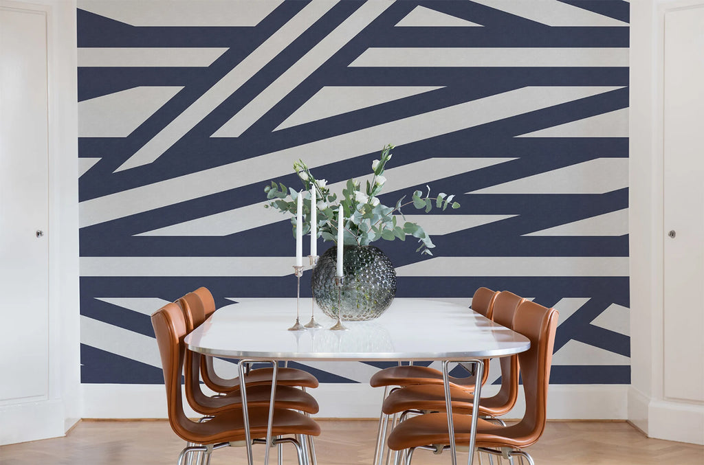 Sailor's Sea, Striped Wallpaper in Dark Blue Colourway featured on a wall of a dining area with white dining table and brown chairs
