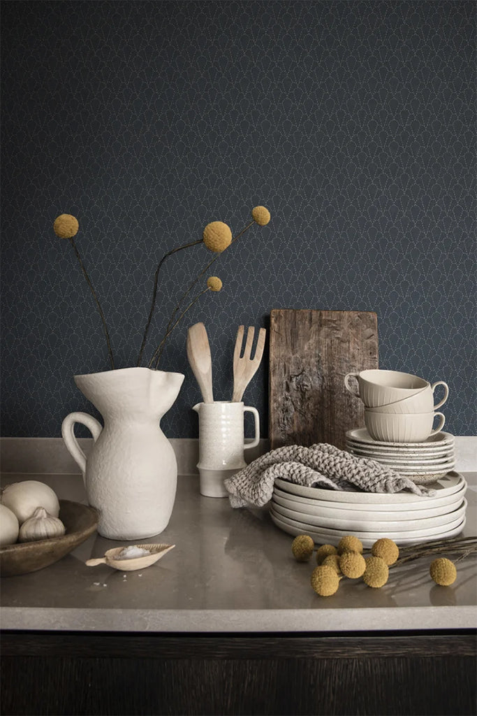 Raphael Floral, Wallpaper in Dark Blue featured on a wall of a kitchen with a table with stacked plates and several kitchenwares on top