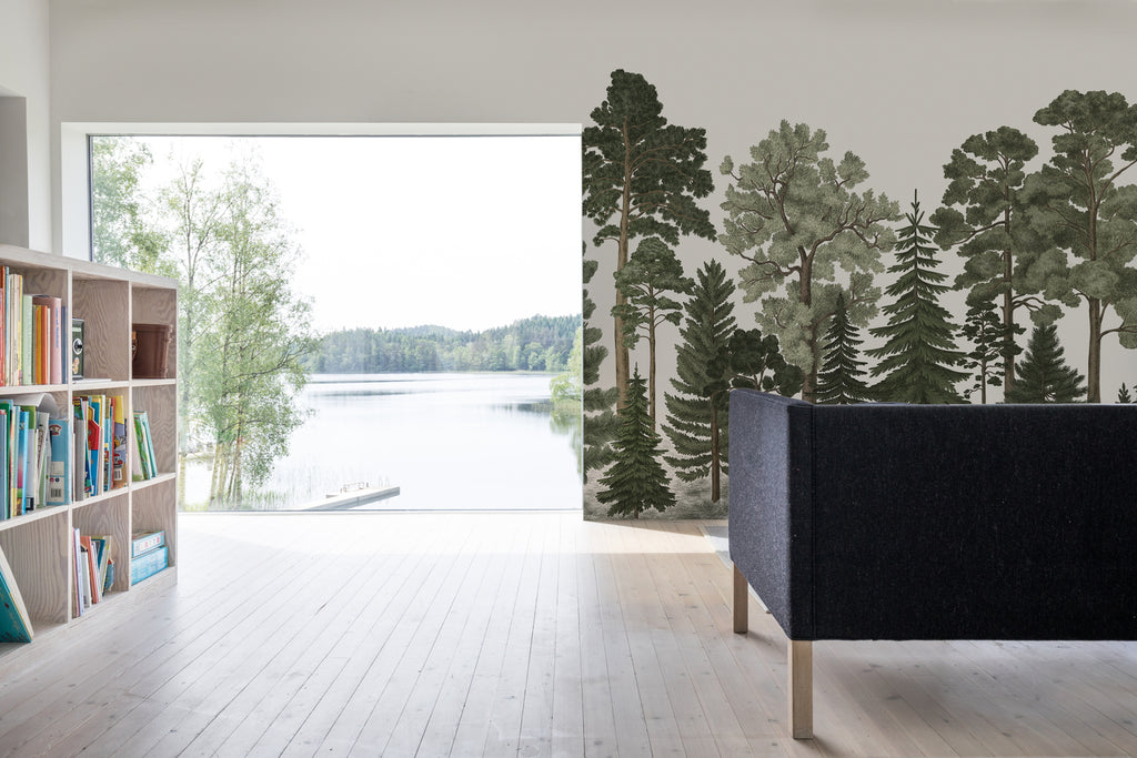 Scandinavian Forest, Mural Wallpaper in forest green as seen on the wall of a living area with large window facing a lake