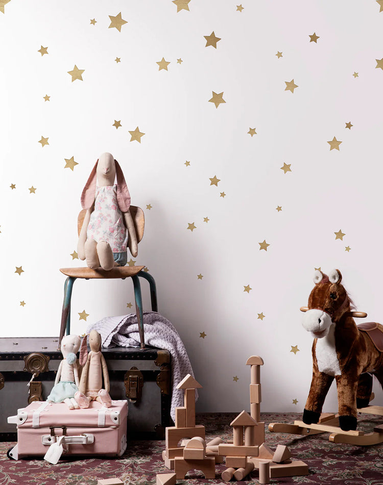 Sky Full of Stars, Pattern Wallpaper in Honey, enhances a room adorned with a lamp, horse plush toys, and blocks scattered on the ground.