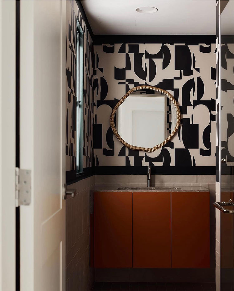A modern bathroom, accentuated by the Slow Assembly Geometric Pattern Wallpaper in Black, features a unique mirror and contemporary amenities. The room’s design, lighting, and decor harmoniously complement the wallpaper’s bold patterns.