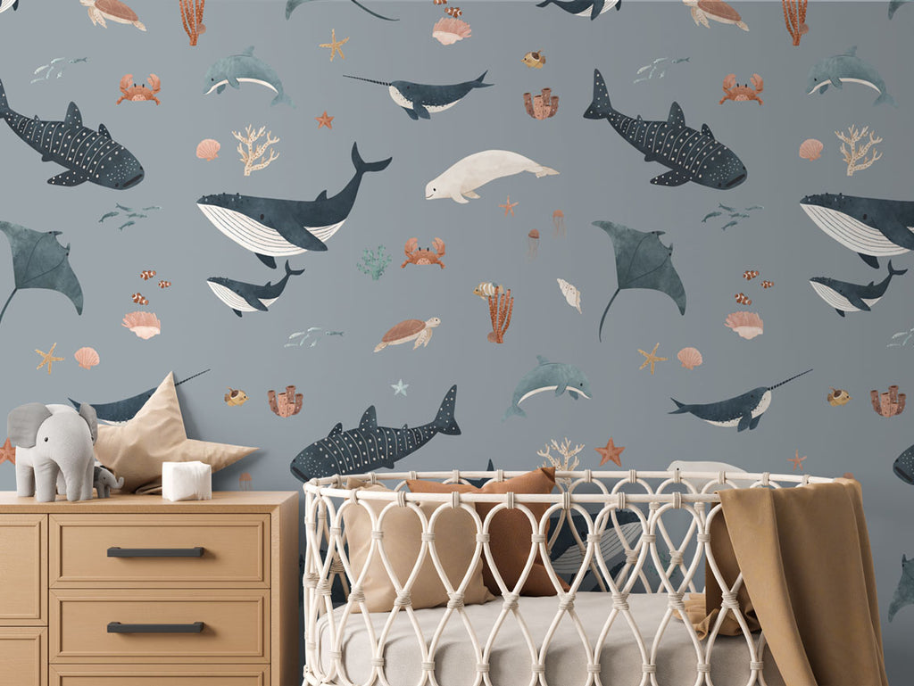 Baby's room with blue Splendid Sea wallpaper, a woven crib, wooden dresser, and ocean-inspired accents for a soothing ambiance.