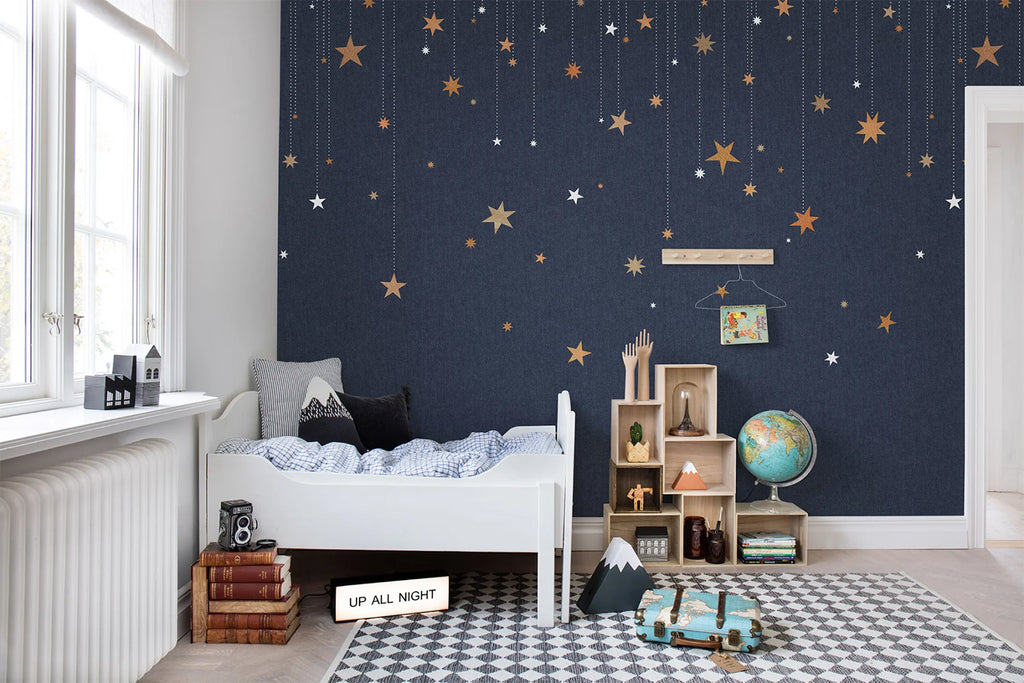 Stargazing, Pattern Wallpaper in Dark Blue featured on a wall of a kid’s bedroom with checkered floor mat and white bed and sheets and scattered toys all around