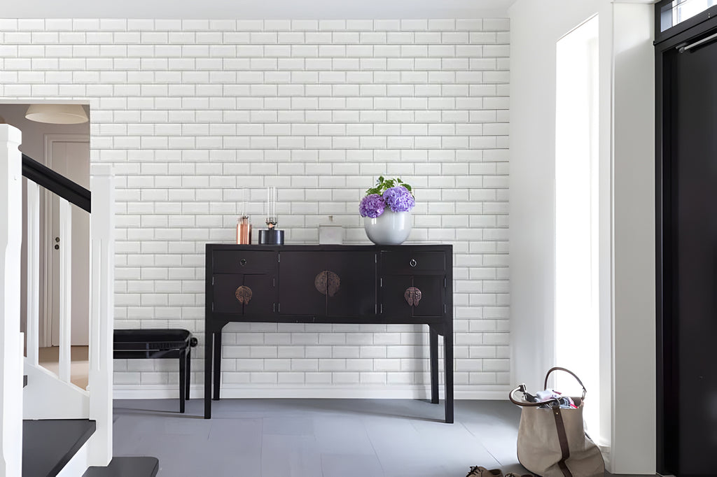 A sophisticated room featuring Subway Tiles, Wallpaper in White, contrasted by a dark floor. A vintage black console table adorns the wall, holding a vase with purple flowers. A staircase with wooden steps ascends on the left, next to a partially visible black chair. A large black door or panel is hinted at on the right.