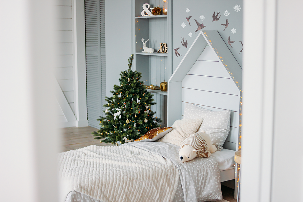 A cozy child’s room adorned with Swallows, Wall Decals. The soft, pastel decals depict graceful swallows in flight, adding a touch of whimsy to the space. The room features a plush toy on a white knitted bed, alongside a decorated Christmas tree adorned with festive ornaments. Warm, gentle lighting completes the inviting ambiance.