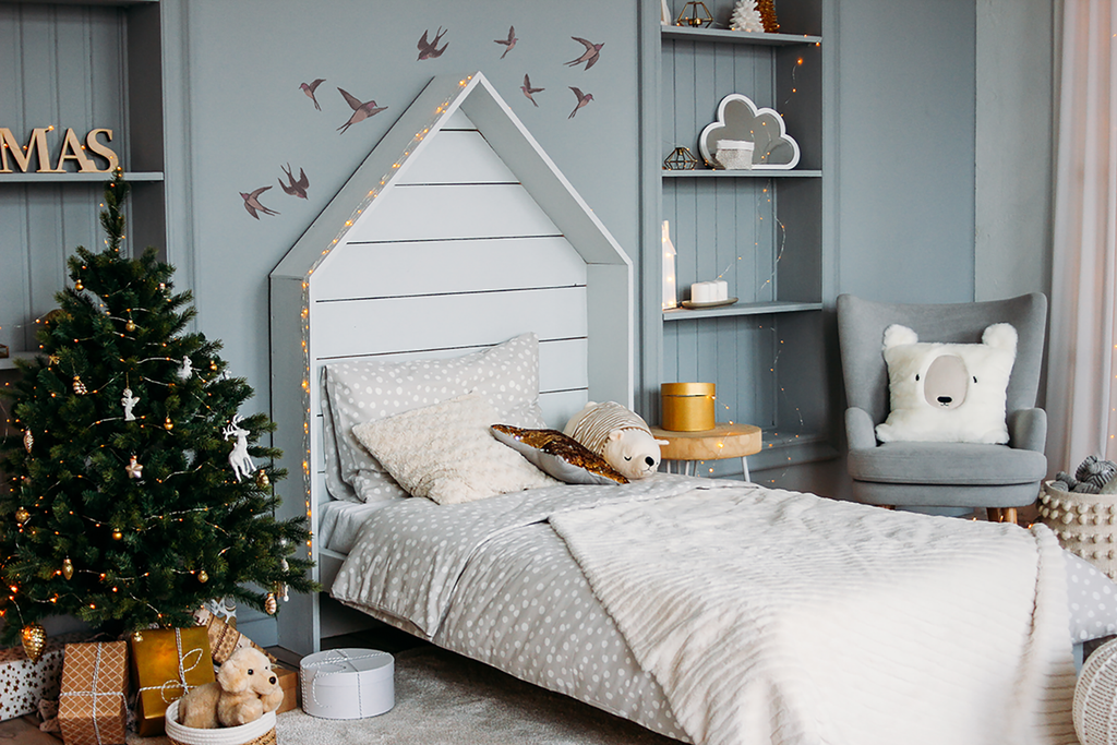 A cozy child’s room adorned with Swallows, Wall Decals. The soft, pastel decals depict graceful swallows in flight, adding a touch of whimsy to the space. The room features a plush toy on a white knitted bed, alongside a decorated Christmas tree adorned with festive ornaments and gifts underneath. Warm, gentle lighting completes the inviting ambiance.