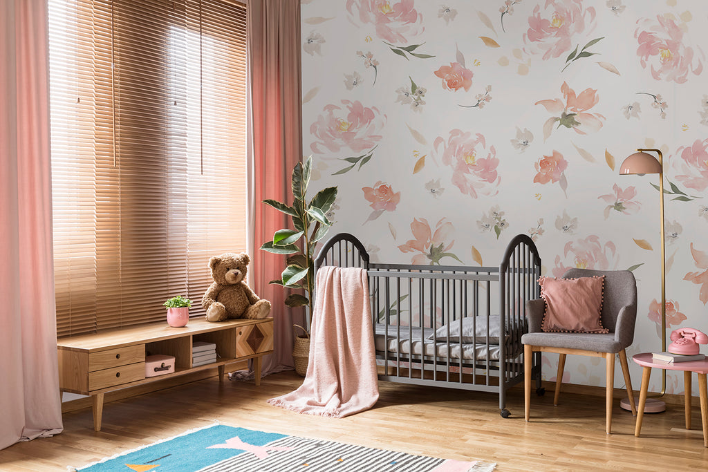 A sunlit nursery with a wooden crib, a plush teddy bear on a bench, an upholstered chair, and a floor lamp. The room features a Sweet Blooms, Pink Floral Pattern Wallpaper.