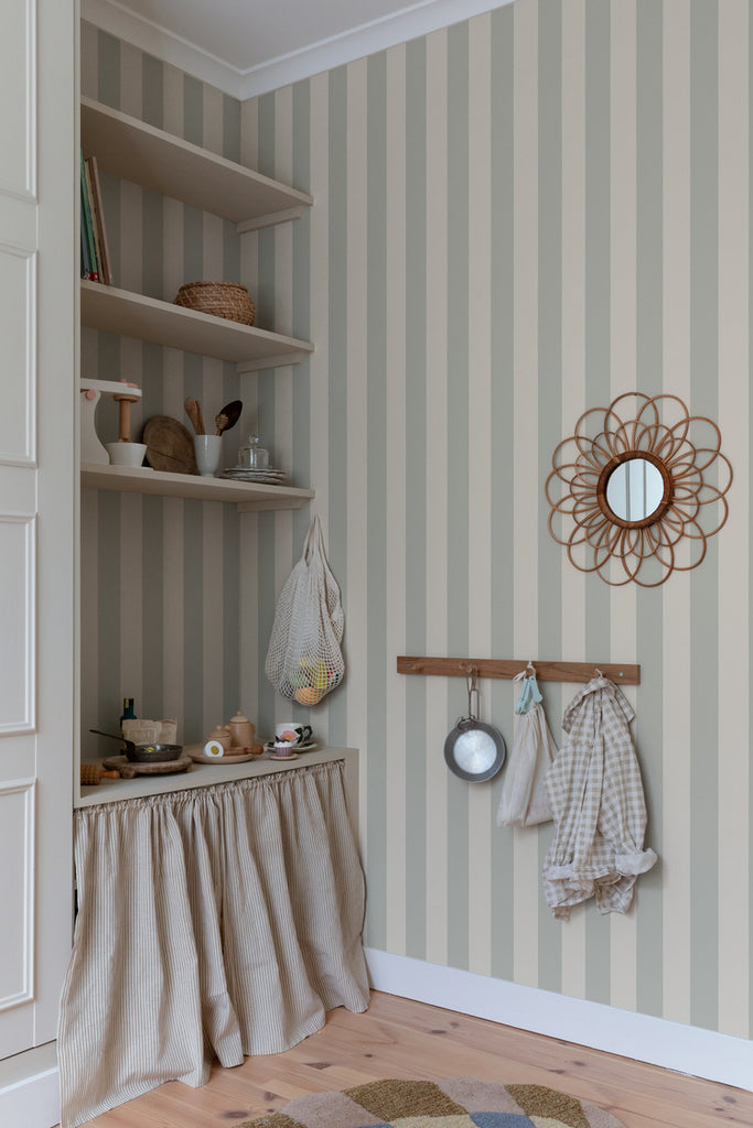 Teira Stripes, Wallpaper in Sage Featured on a wall of a room with shelves with several items on top of it. 