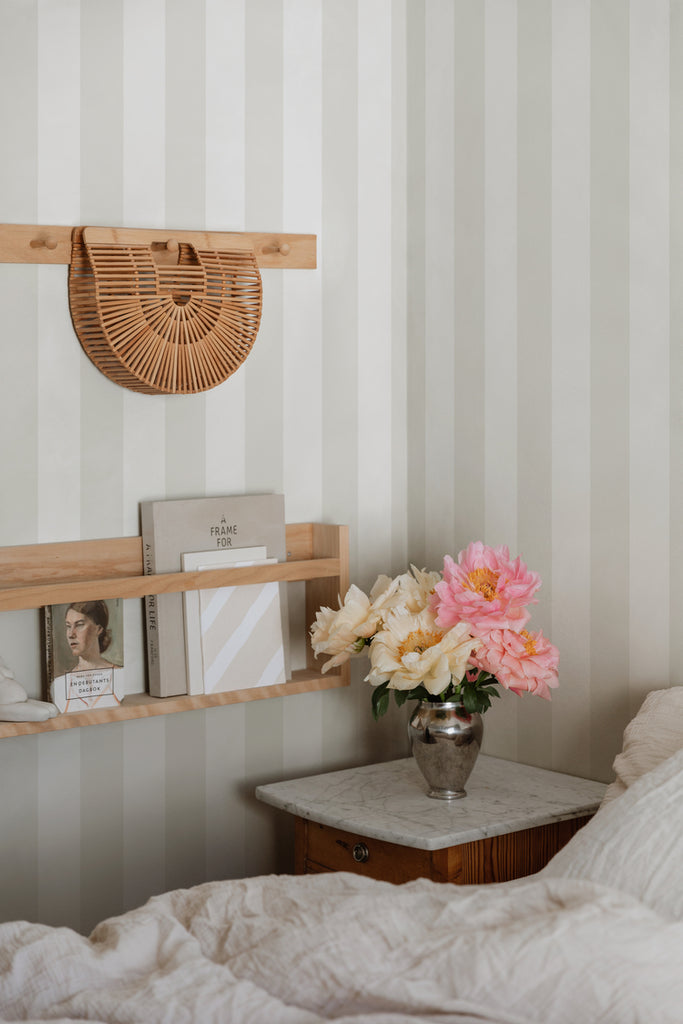 Teira Stripes, Wallpaper in Sand Featured on a wall of a bedroom with a side table with flowers on top of it and a bed with white sheets and pillows