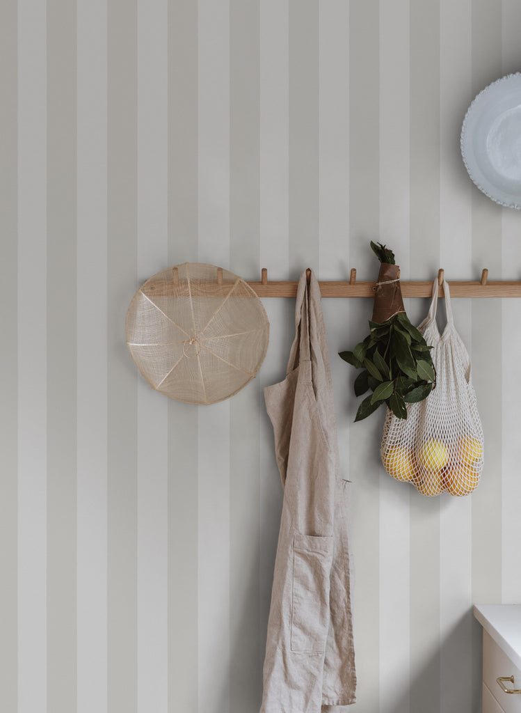 Teira Stripes, Wallpaper in Sand Featured on a wall of a room with flowers, groceries and apron hanging on its walls