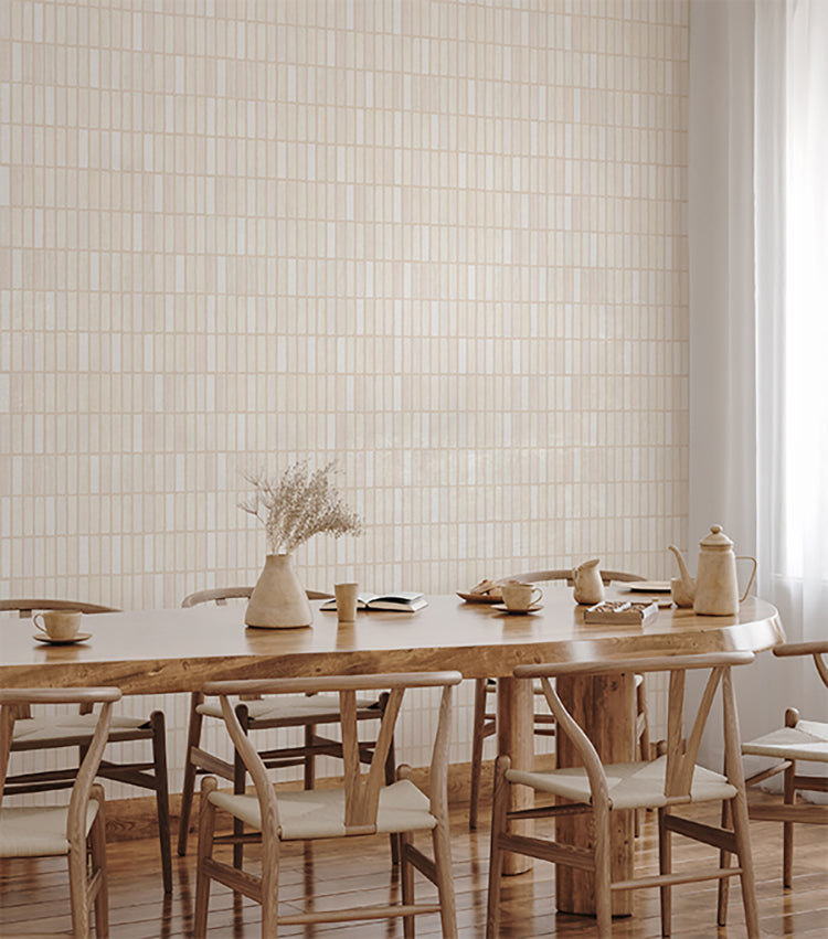 A bright, airy room bathed in natural light, featuring a wooden dining table set with ceramic dishes. Dried flowers in a vase add a touch of decor. The walls, adorned with Terra Tessel, Pattern Wallpaper in Beige, enhance the room’s serene aesthetic.