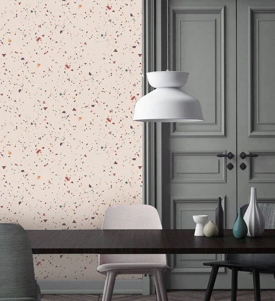 Terrazzo Kie, Wallpaper in nude is featured on a wall of a dining area, which is furnished with a dark wood table and multiple uniquely designed chairs. Above the table hangs a white pendant light