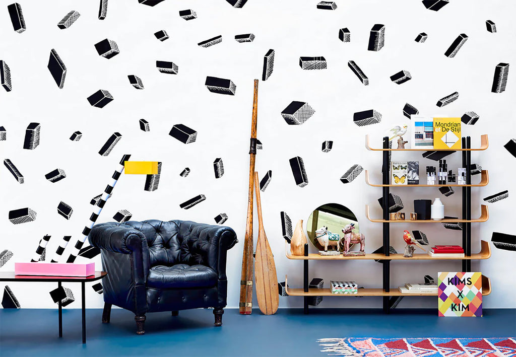 A stylish room with Tetris, Pattern Wallpaper in Black/White, a modern black couch, a wooden shelf with various items, and colorful wall art creating a contemporary aesthetic.