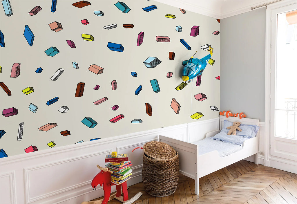 A child’s bedroom enlivened by a Tetris, Pattern Wallpaper in Multicolor, featuring a variety of playful shapes. The room includes a white bed with plush toys and a small bookshelf.
