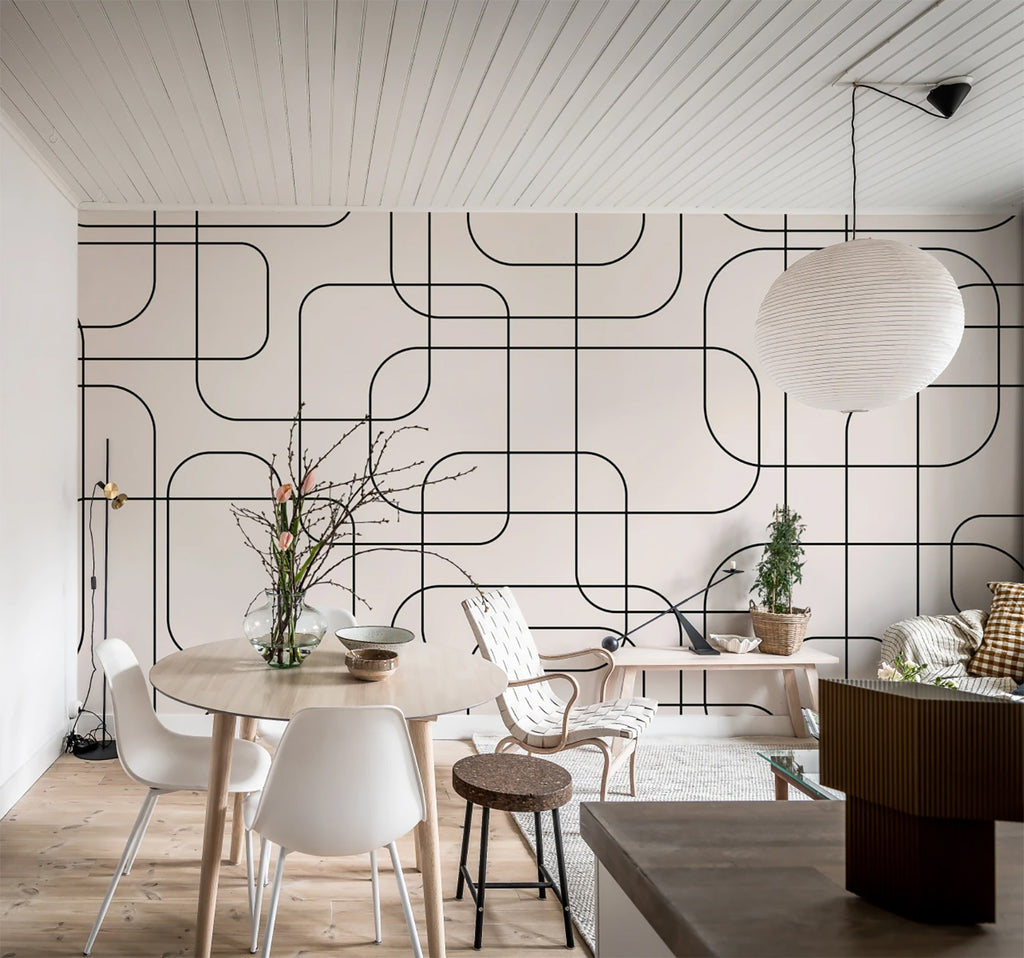 Thea Graphic lines, Pattern Wallpaper in Beige featured in a living area with several white chairs, wooden round table with a vase with plant, and wooden flooring.