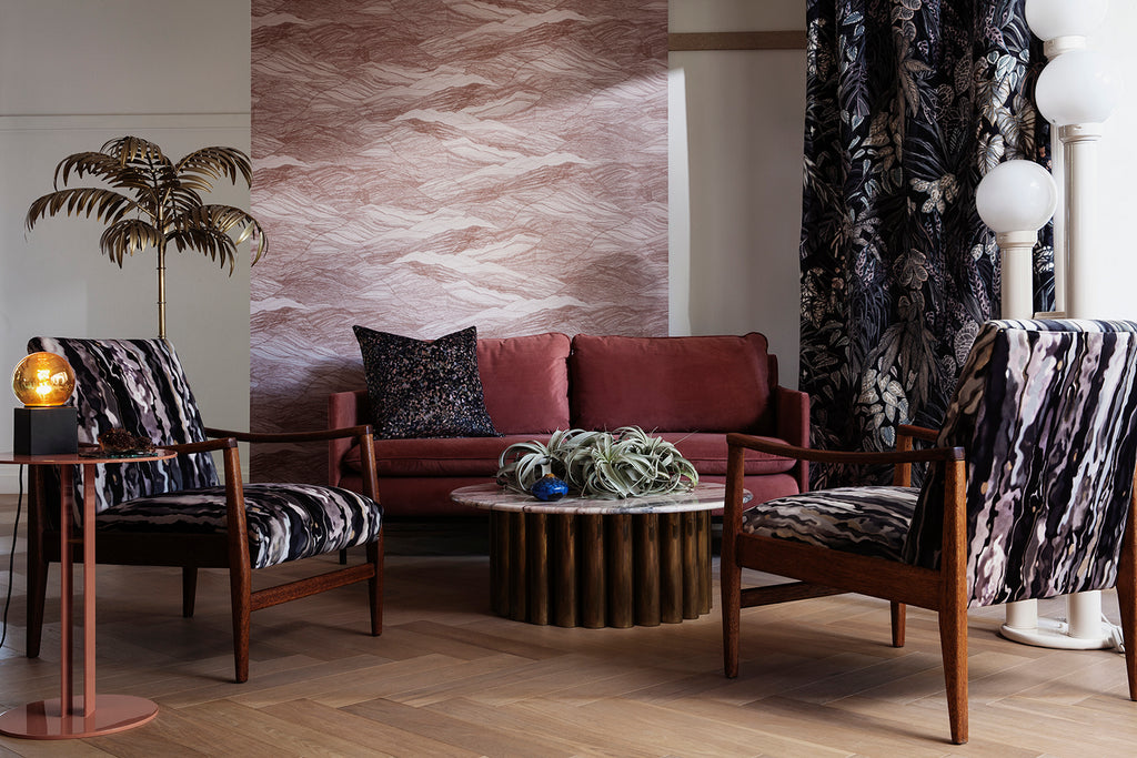 Tidal Waves Wallpaper in Terracotta graces a living area where it is complemented by black curtains and a stylish black foamed wooden chair, resulting in a bold and sophisticated interior.