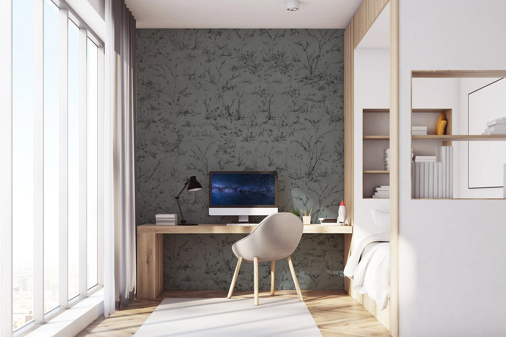 Trisha Floral Pattern Wallpaper, in a sophisticated grey tone, is displayed on a wall of a room. The room is furnished with a computer table that holds a desktop set, positioned next to a white bed.