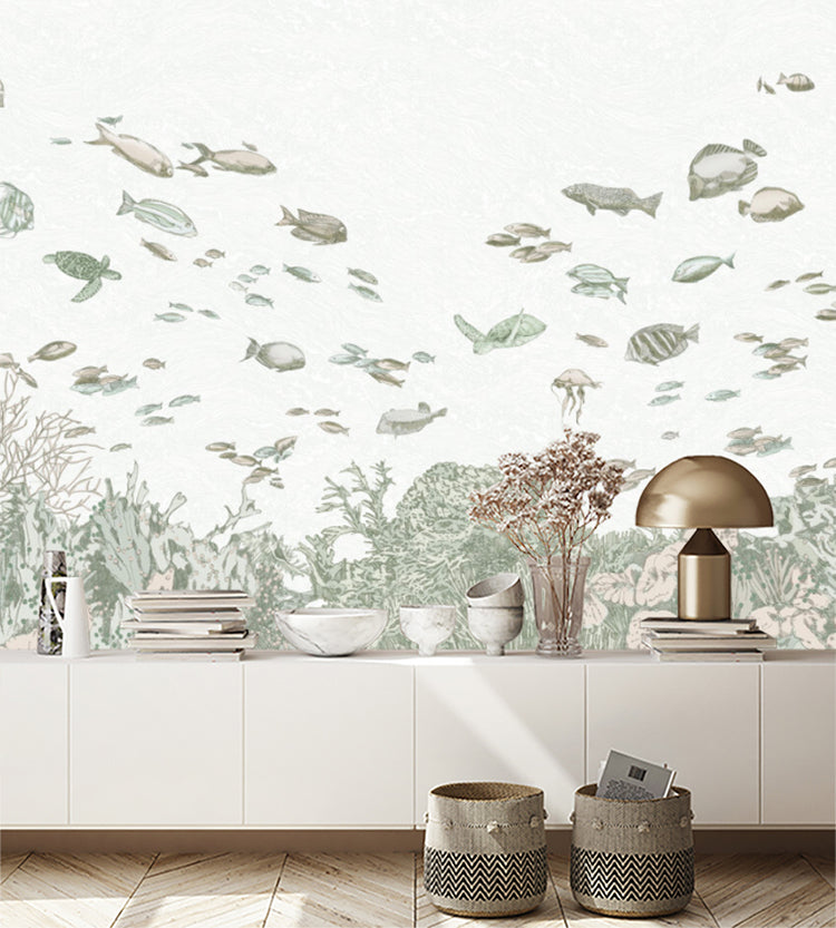 Under the Sea, Wallpaper in sand, adorns a room featuring a long white table that has been artfully arranged with stacked books, ceramic kitchenware, and a glass vase filled with vibrant flowers. A bronze lamp adds a touch of elegance. On the ground, two baskets contribute to the room’s organized charm. 