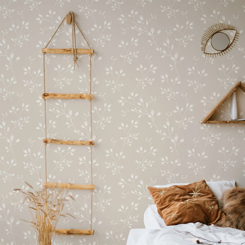 A cozy corner in a room with Vintage Wildflower pattern wallpaper. Features include a decorative ladder, a golden eye-shaped mirror, a wooden triangle shelf, and a glimpse of a bed with white bedding.