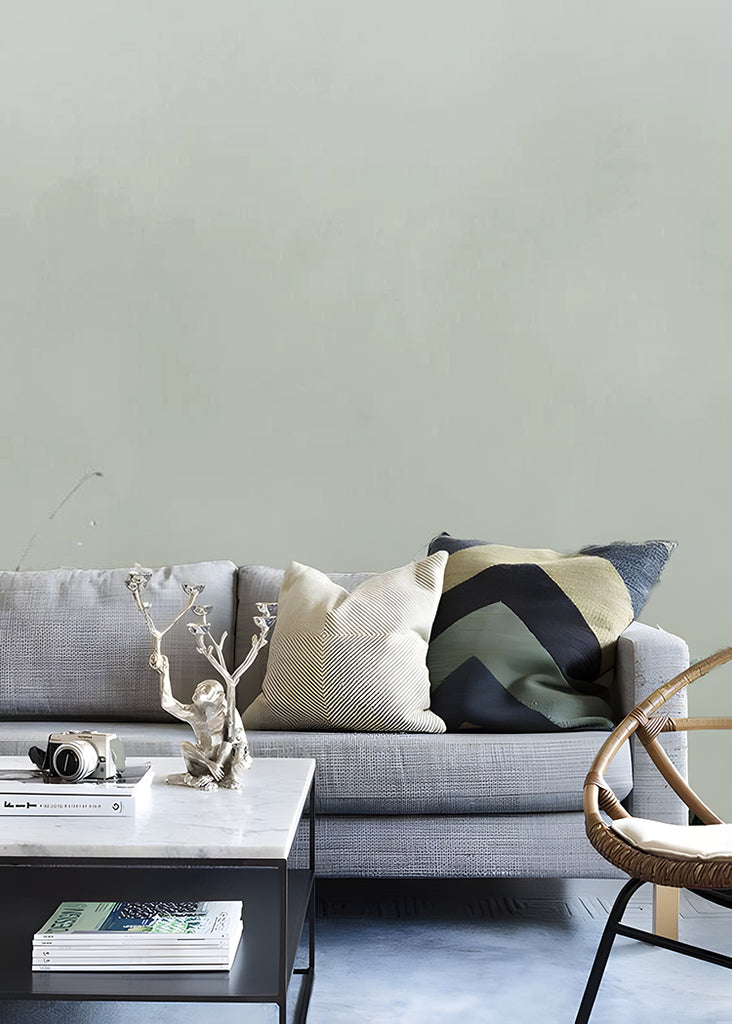 A green Watercolour Gradient Ombre Mural Wallpaper is featured on a wall, complemented by a grey sofa adorned with variously designed pillows. Adjacent to the couch, a marble-textured coffee table and a rattan chair complete the setting.