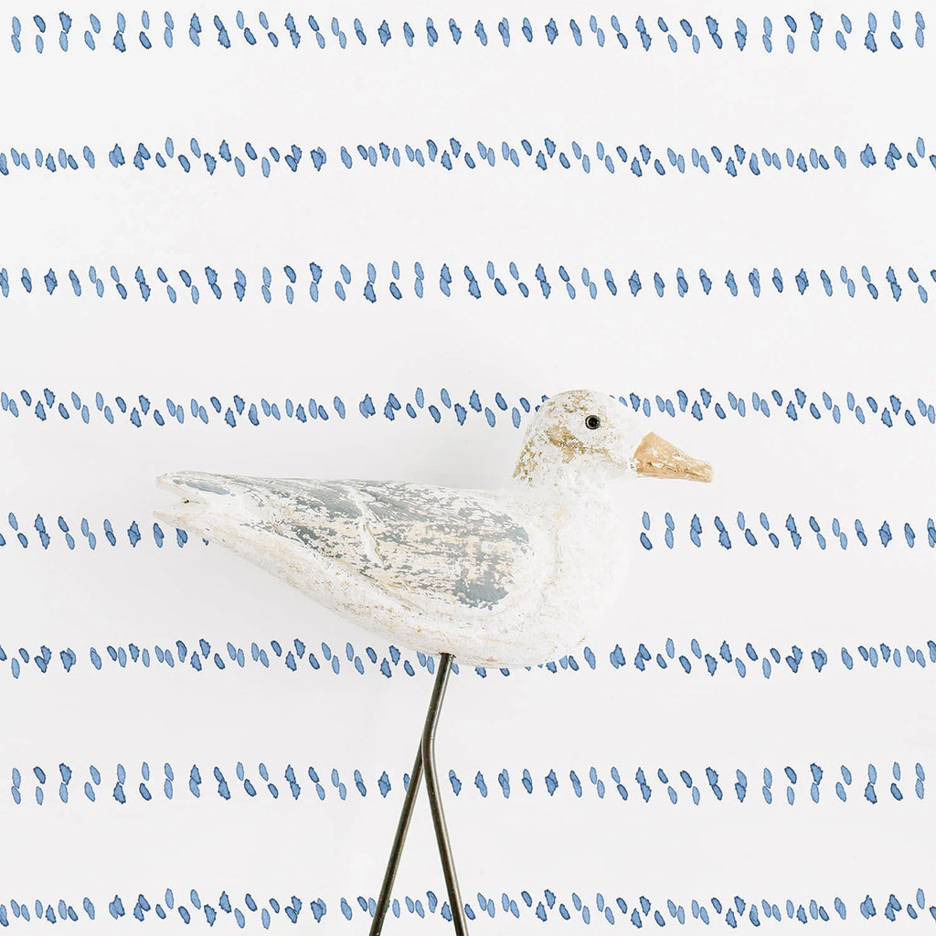 An antique white bird figurine perched on a thin metal rod, set against a serene ‘Watercolour Spot Lines’ wallpaper. The wallpaper features an abstract pattern of blue spots and lines on a white backdrop, reminiscent of tranquil watercolor strokes.