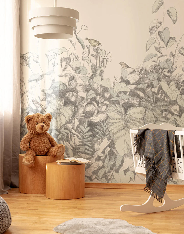 Willow Bush, Wallpaper in grey, enhances a kid’s room wall. A white crib with a grey blanket, a stuffed animal on a wooden cylindrical chair, and a white pendant light are all visible.