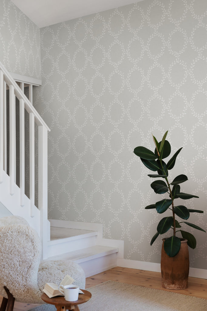 Wilma Wreath Patterned Wallpaper in Grey Featured on a wall near a staircase with  wooden flooring and a planter along the way