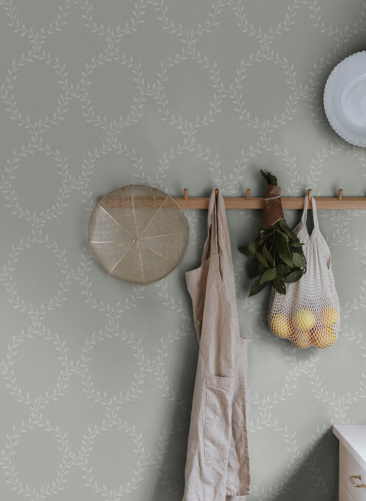 Wilma Wreath Patterned Wallpaper in Sage Featured on a wall with apron and groceries hanging