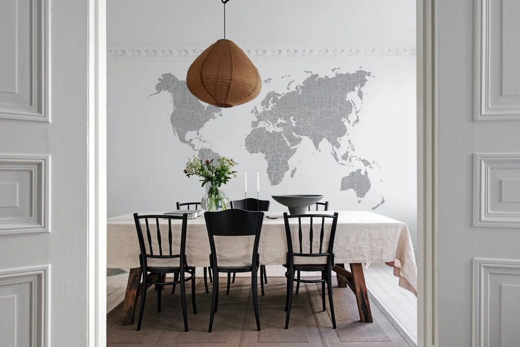Your Own World Map, Mural Wallpaper in grey featured on a wall of  a dining area with a wooden dining table, pendant lights and black dining chairs