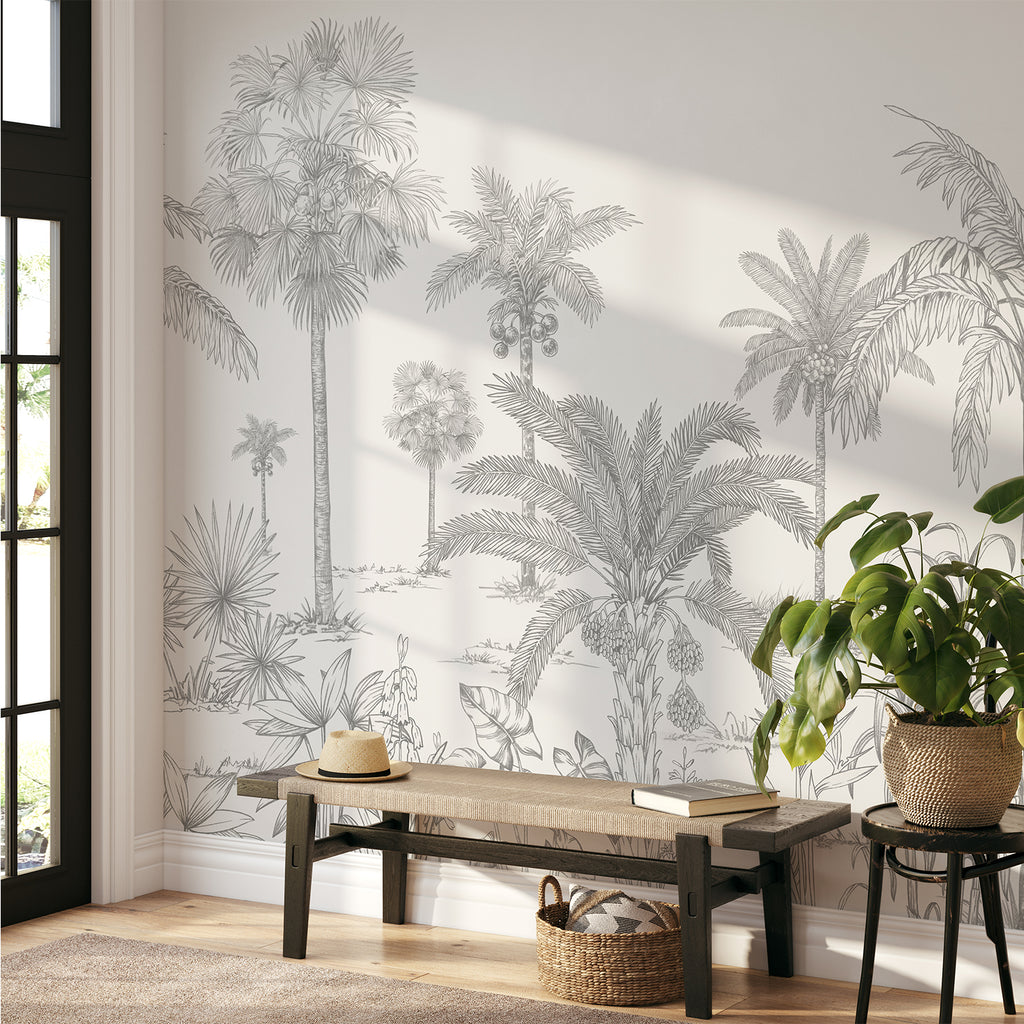 A serene room adorned with the Vintage Palmscape, Tropical Mural Wallpaper in Grey. Detailed palm tree illustrations grace the walls, creating a tranquil ambiance. A sleek wooden bench holds a lamp, books, and vases, seamlessly complementing the tropical theme.