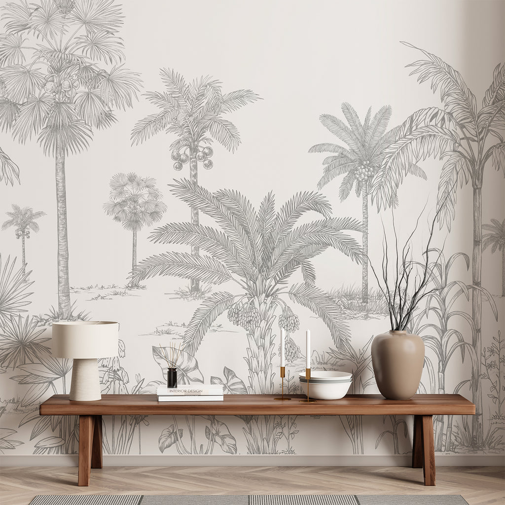 A hallway adorned with the Vintage Palmscape, Tropical Mural Wallpaper in Grey. The monochrome mural depicts various palm trees and tropical foliage. The minimalist decor includes a wooden bench, a woven basket, potted plants, and a large window that bathes the space in natural light.