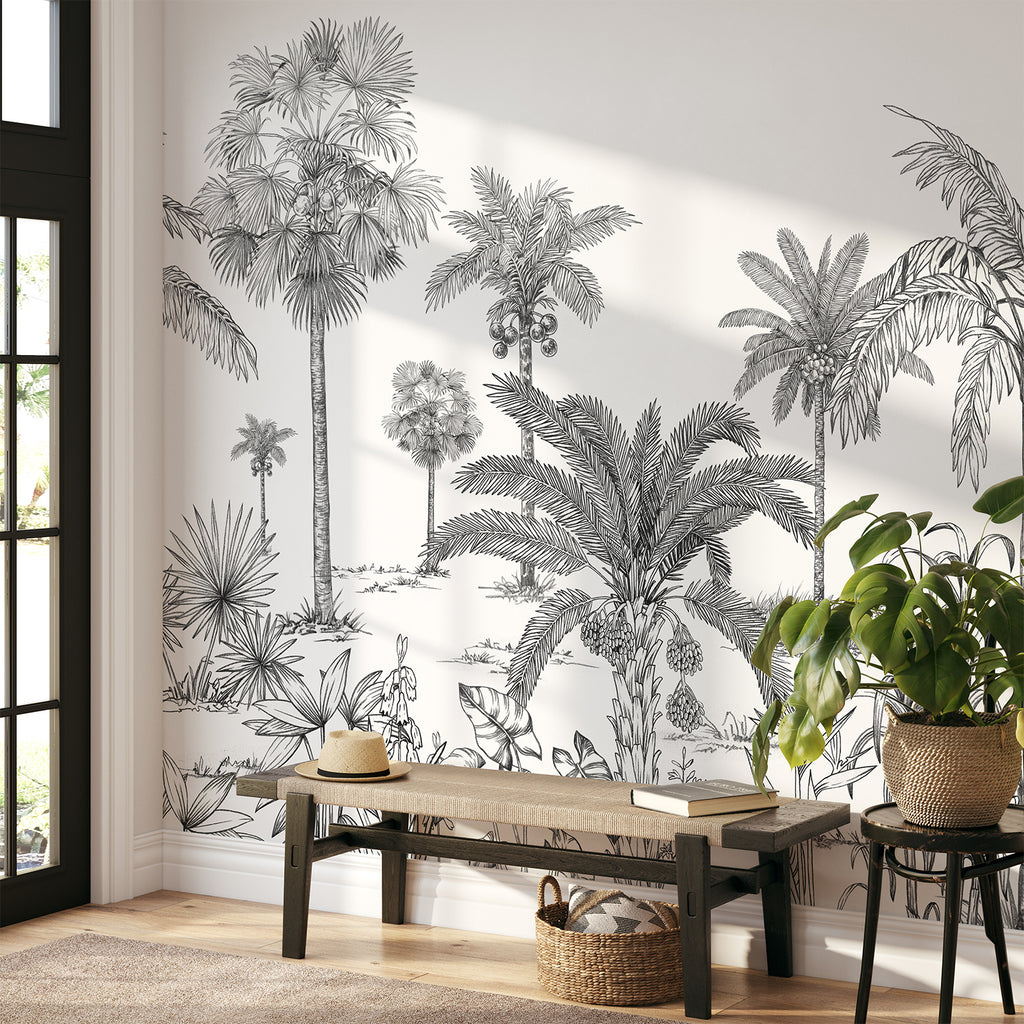 A serene room adorned with the Vintage Palmscape, Tropical Mural Wallpaper in Black White. Detailed palm tree illustrations grace the walls, creating a tranquil ambiance. A sleek wooden bench holds a lamp, books, and vases, seamlessly complementing the tropical theme.
