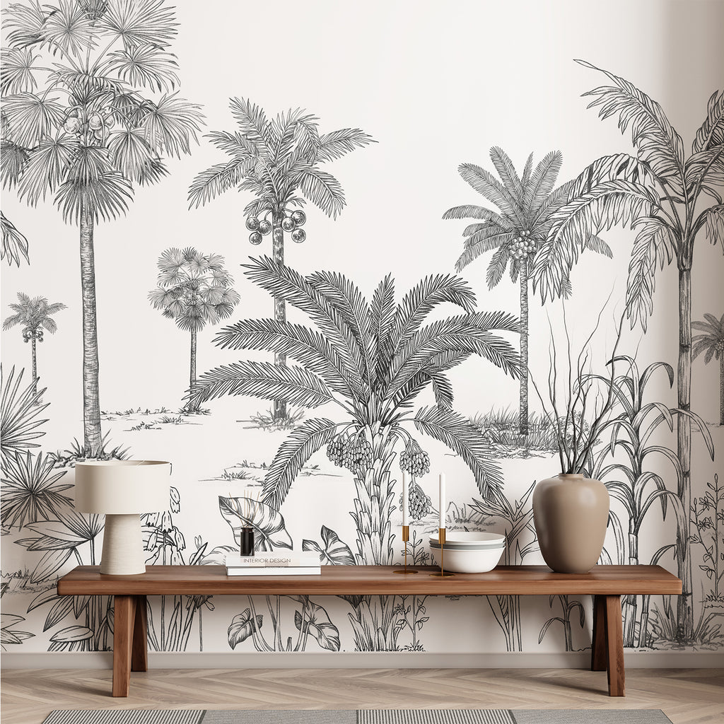 A hallway  adorned with the Vintage Palmscape, Tropical Mural Wallpaper in Black White. The monochrome mural depicts various palm trees and tropical foliage. The minimalist decor includes a wooden bench, a woven basket, potted plants, and a large window that bathes the space in natural light.