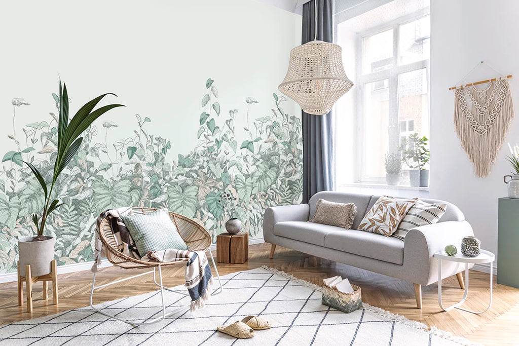 Willow Bush jungle wallpaper with soft layered ferns and foliage behind a grey sofa and woven rug in a bright living room
