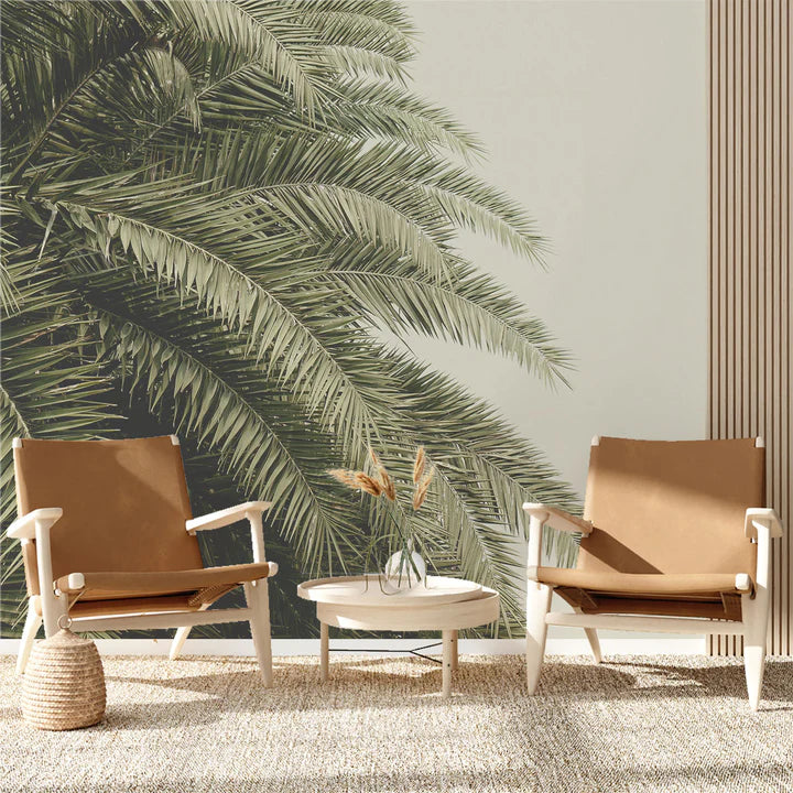Leaf Love jungle wallpaper with oversized green palm fronds across a pale wall behind two tan leather lounge chairs