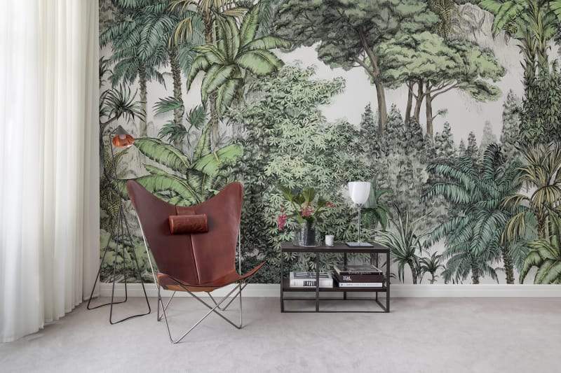Secret Garden jungle wallpaper with lush layered tropical trees and palms behind a leather butterfly chair and side table