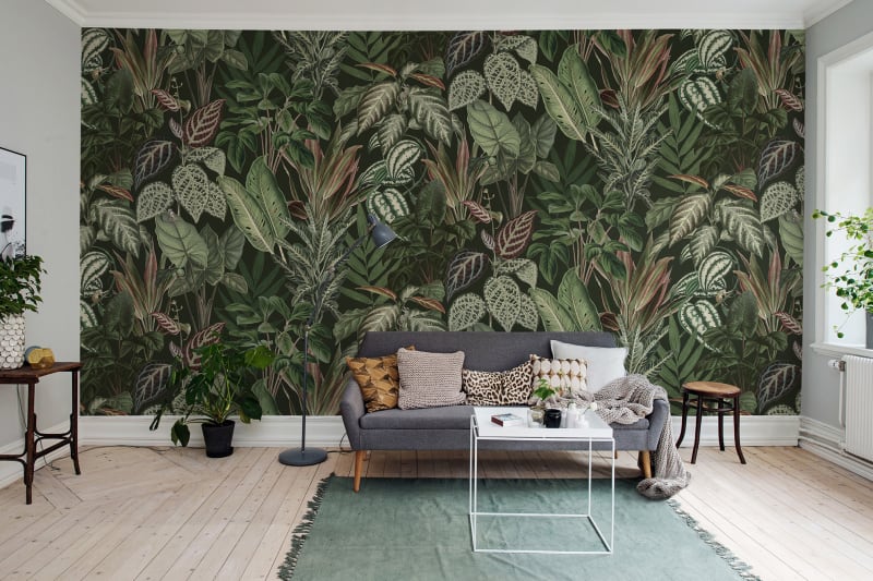 Night-time Jungle wallpaper with dense dark green tropical foliage behind a pale sofa and green rug in a living room