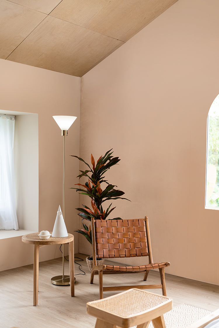 A serene room featuring a Calbri Ombre Wallpaper, a stylish leather chair, a round table with decor, an indoor plant, and a floor lamp near a window with sheer curtains.